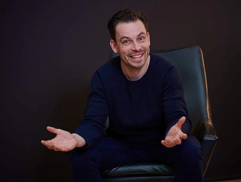 Man genaamd Mark zit lachend in een stoel met open handgebaren tegen een donkere achtergrond | Mr Cashflow
